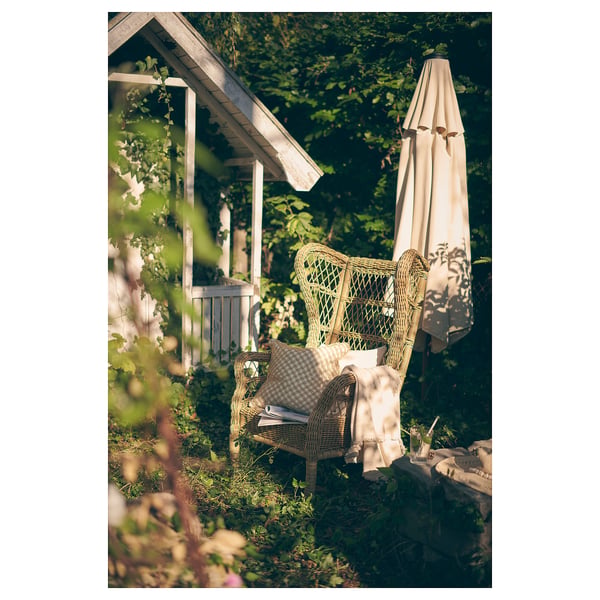 Grüner RISHOLMEN Korbstuhl im Garten mit offenem Sonnenschirm.
