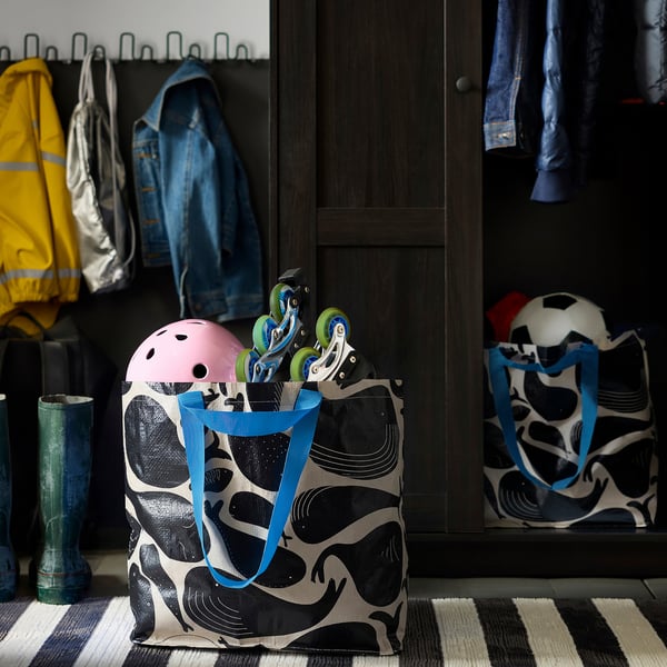 Große Romeson-Tasche mit blauen Henkeln auf einer gestreiften Matte neben den Stiefeln und dem Schrank.