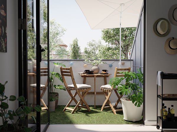 Moderner Balkon mit grünem RUNNEN-Gras , Holzstühlen und Pflanzen. Großes Fenster und weißer Sonnenschirm.