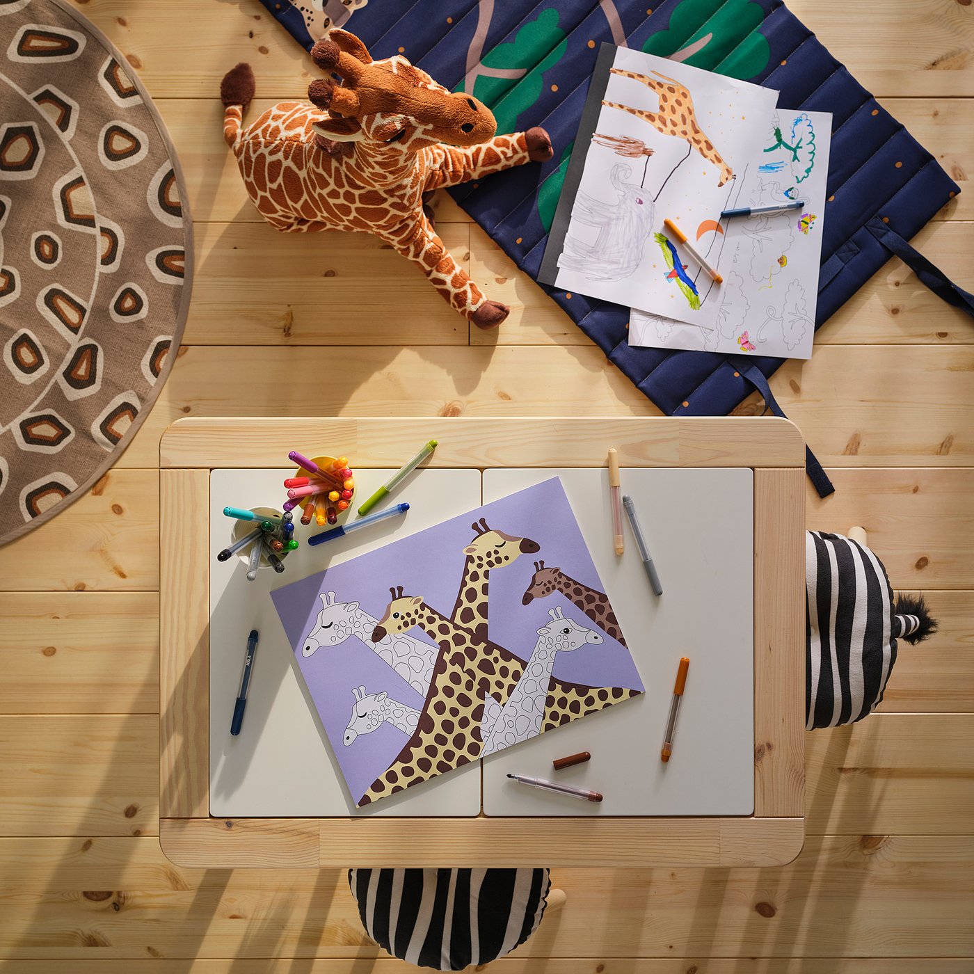 Spielbereich zum Thema Giraffe mit Kuscheltier, blauer Decke, Malvorlage und Zebrakissen.