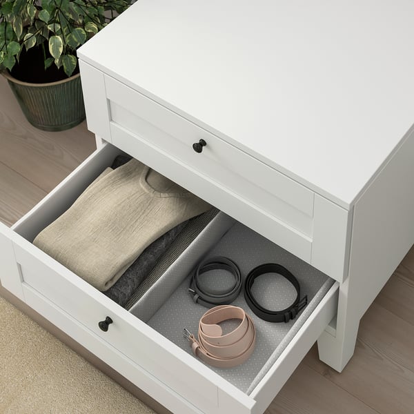 Offene weiße Schublade mit Gürteln und gefalteter Kleidung.
