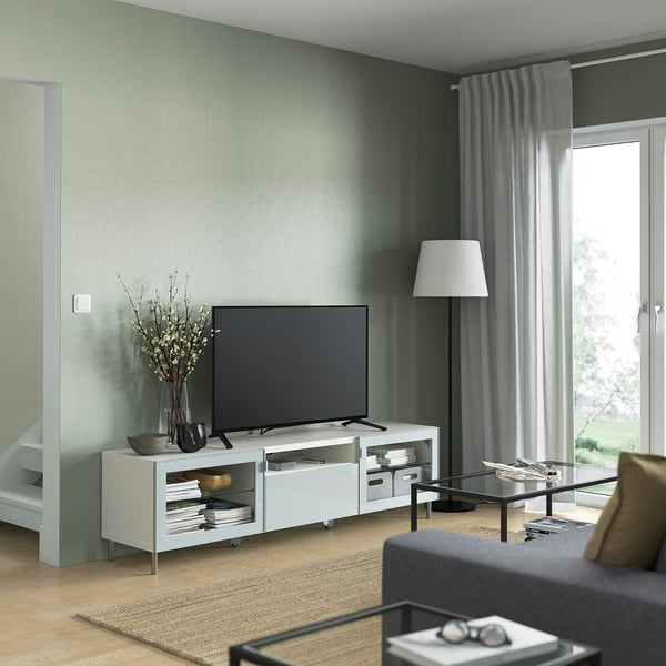 Wohnzimmer mit großem Fernseher, grauem Sofa und Couchtisch aus Glas vor grüner Wand.