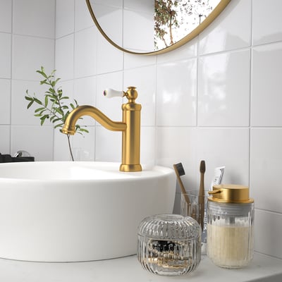 Goldener Wasserhahn, weißes Waschbecken, runder Spiegel, Toilettenartikel, SILVTJÄRN Seifenspender. Glas sorgt für Luxus.