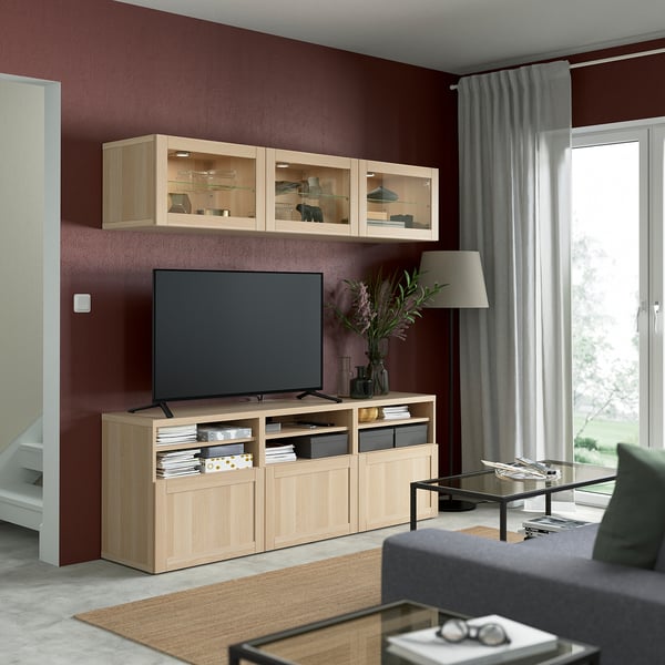 Großes, modernes Wohnzimmer mit roten Wänden, SINDVIK TV-Ständer aus heller Eiche und Glasschrank, grauem Sofa, Couchtisch und großem Flachbildfernseher.