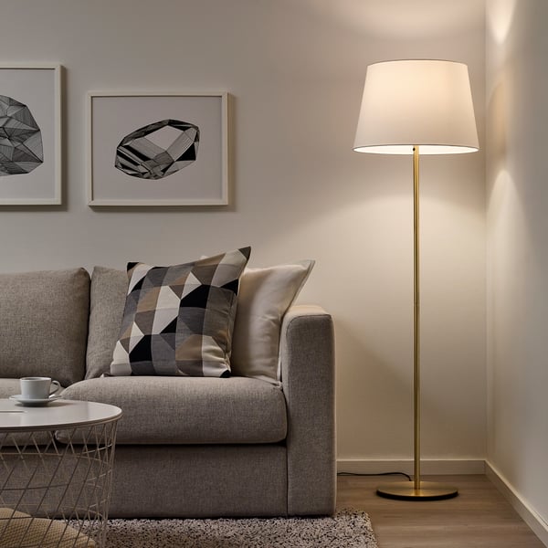 Minimalistisches Wohnzimmer mit grauem Sofa, moderner Stehlampe, cremefarbenem Lampenschirm, Couchtisch und abstrakter Wandkunst.