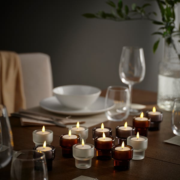 Holztisch mit SKATGÅS Teelichtern und grüner Vase. Oder, um das Gedeck einzubeziehen: Holztisch mit SKATGÅS Teelichtern , Grün und Gedeck.