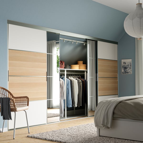 Modernes blaues Schlafzimmer mit grauem Bett, SKYTTA verspiegelte Schranktür, Kleidung sichtbar.
