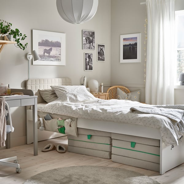 Kinderzimmer mit weißem Bett, Korbstuhl und Fotos.