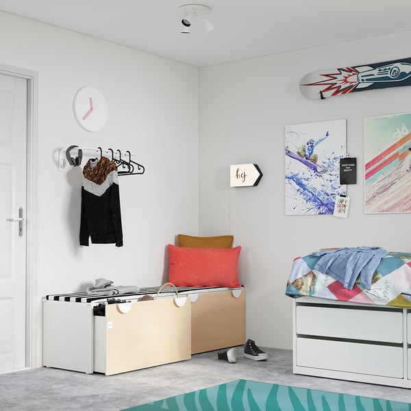 Helles Schlafzimmer mit farbenfroher Kunst, mehrfarbigem Bett, Holzbank mit Boxen, roten und braunen Kissen.