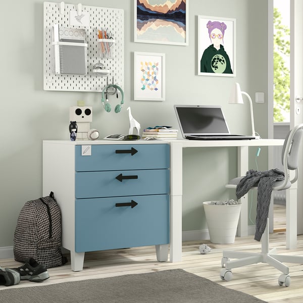 Modernes Homeoffice mit weißem und blauem SMÅSTAD-Schreibtisch, Laptop, grauem Stuhl, farbenfrohen Kunstwerken, Kopfhörern und Rucksack.