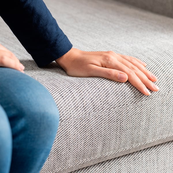 Nahaufnahme einer Hand, die auf einem weichen, strukturierten grauen Sofa ruht und dessen Komfort und hochwertige Polsterung hervorhebt.