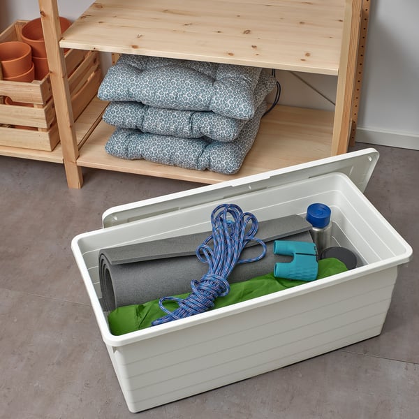 Öffne die Plastikbox mit grünem Tuch, Seil und Wasserflasche. In der Nähe eines Regals mit Kissen und Pflanzen.
