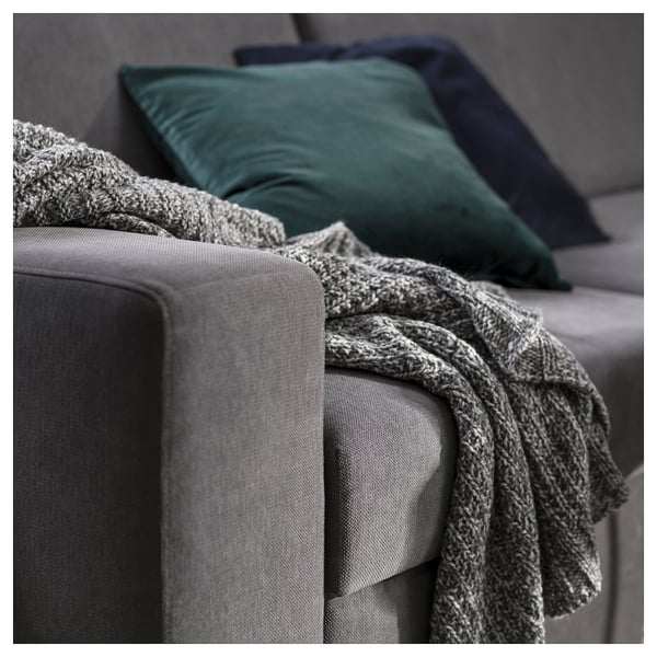 Gemütliches graues Sofa mit strukturierter Decke und grünen Kissen.