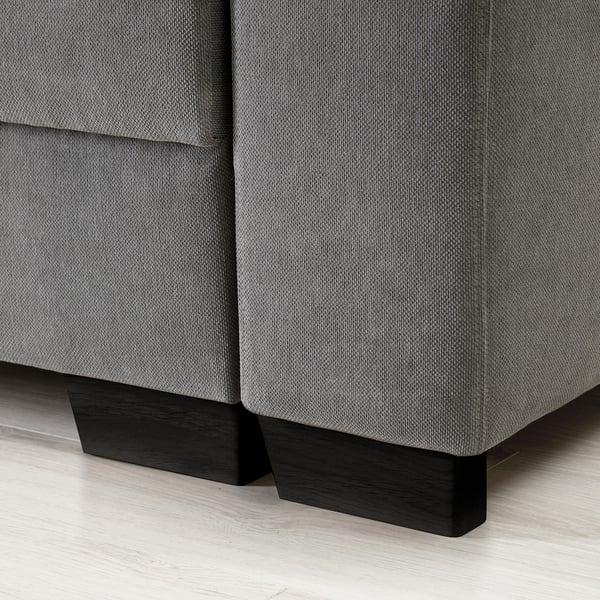 Eine moderne Sofaecke, gepolstert mit grauem Stoff, mit schlanken schwarzen Holzbeinen.