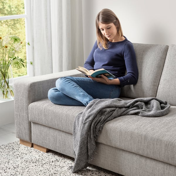 Eine Frau liest auf einem grauen SÖRVALLEN-Sofa am Fenster. Das Sofa hat eine Liege und einen leichten, modernen Look.