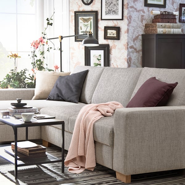 Modernes Wohnzimmer mit hellgrauem SÖRVALLEN-Sofa, dekoriert mit Kissen und einem Überwurf, in der Nähe eines kleinen Tisches mit einer Tasse Tee und einem Buch.