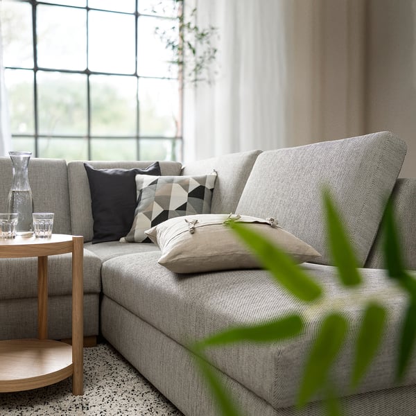 Modernes graues SÖRVALLEN-Sofa, minimalistisches Design mit schwarzen und weißen Kissen, Beistelltisch aus Holz und grüner Pflanze, in der Nähe des großen Fensters.