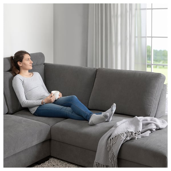 Frau entspannt sich auf SÖRVALLEN Sofa mit Becher, Decke in der Nähe.