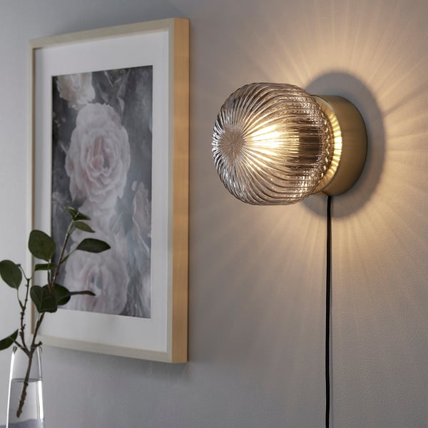 Moderne Wandleuchte aus glänzendem Messing mit grauem Glasschirm, der weiches Stimmungslicht ausstrahlt.
