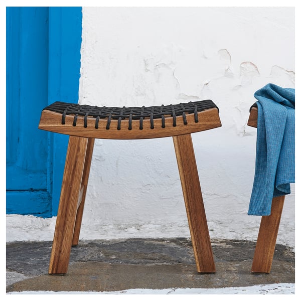 Zwei Holzhocker mit geflochtenen Sitzen, die an einer weißen Wand und einer blauen Tür platziert sind.