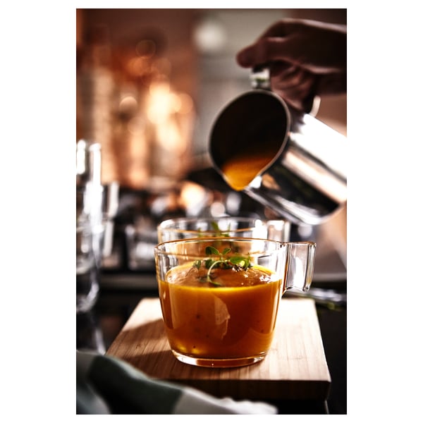 Barista gießt Orangengetränk in einen Klarglasbecher auf der Holzarbeitsplatte.