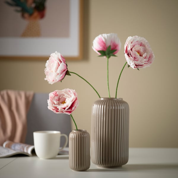 Beige Steingutvase mit rosa Blumen und Tasse auf dem Tisch.