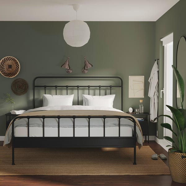 Modernes Schlafzimmer mit schwarzem Bett, weißer Bettwäsche, grünen Wänden, grauem Nachttisch, Kunst und Lichtern.