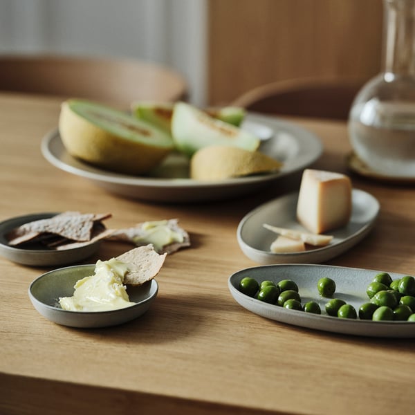 Kleine Teller mit Brot, Käse, Erbsen und Soße auf einem Holztisch.