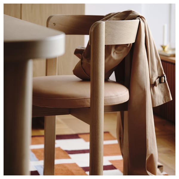 Heller Holzstuhl mit Sitz und Rückenlehne aus beigem Leder und Jacke, die über die Rückenlehne drapiert ist. Mit modernem skandinavischem Design und Komfort.