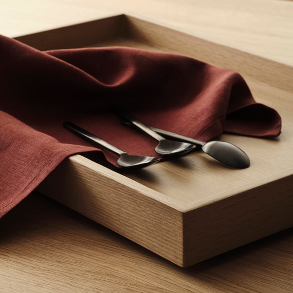 Holztablett mit dunkelrotem Tuch und Metalllöffeln, das hochwertige Verarbeitung und Handwerkskunst zeigt.