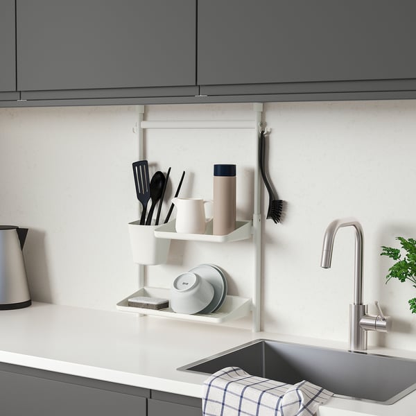 Moderne Küche mit grauen Schränken, hängenden weißen SUNNERSTA-Organizern, in denen Utensilien, Tassen und Schwämme in der Nähe eines stilvollen silbernen Wasserhahns aufbewahrt werden.