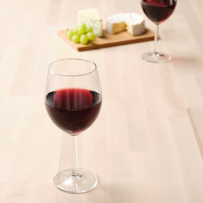 Zwei Weingläser mit Rotwein auf einem Holztisch. Ein Glas neben einer Käseplatte mit Trauben und Käse.