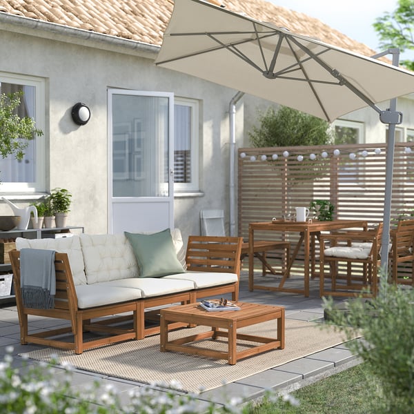 Hinterhofterrasse mit Holzmöbeln, weißen Kissen, großem beigem Sonnenschirm und Lichterketten.