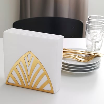 Goldener Serviettenhalter mit weißen Servietten, Stapeln von Tellern und Gläsern auf dem Tisch.