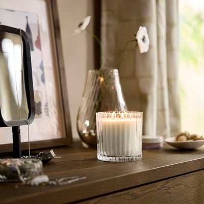 Holztisch mit brennender TOFSTÄRNA-Kerze , Glasvase mit Blumen, Schmuck und Spiegel.