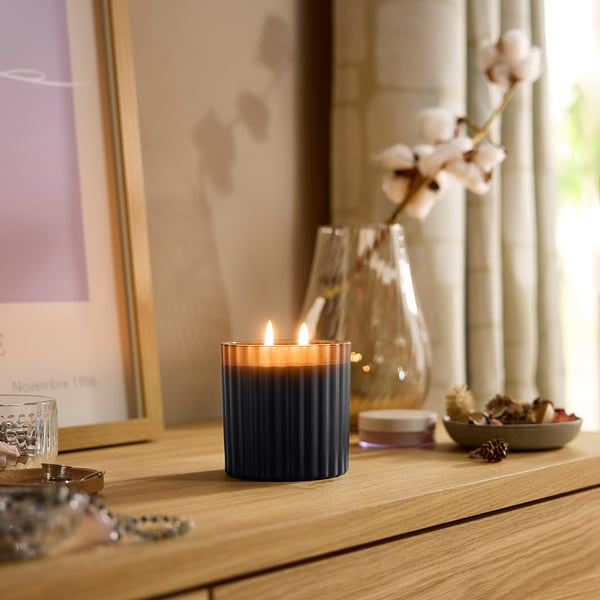 Gemütliches Interieur mit einer TOFSTÄRNA-blauen Kerze auf einem Holzregal, umgeben von Dekoartikeln.