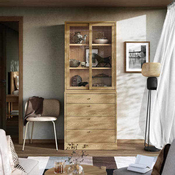 Eichenschrank mit Glasschiebetüren und 4 Schubladen. In der Nähe ein Stuhl mit einer Decke, einer Lampe, einem Bild und einem Couchtisch aus Glas.