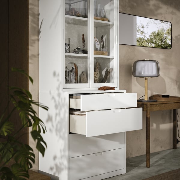 Modernes Zimmer mit weißem TONSTAD-Schrank und -Truhe, Glastüren, Holzschreibtisch, Lampe und Pflanze.