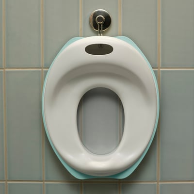 Ein weiß-türkisfarbener Kinder-Toilettensitz, der auf Komfort ausgelegt ist und an einer gefliesten Wand befestigt ist.