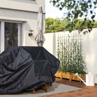 Hinterhofszene: Die TOSTERÖ-Abdeckung schützt einen Tisch im Freien mit einer Gießkanne, Pflanzen und Glastüren in einer ruhigen grünen Umgebung.