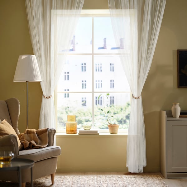 Wohnzimmer mit großem Fenster, Sessel, Beistelltisch, Pflanze und Lampe.