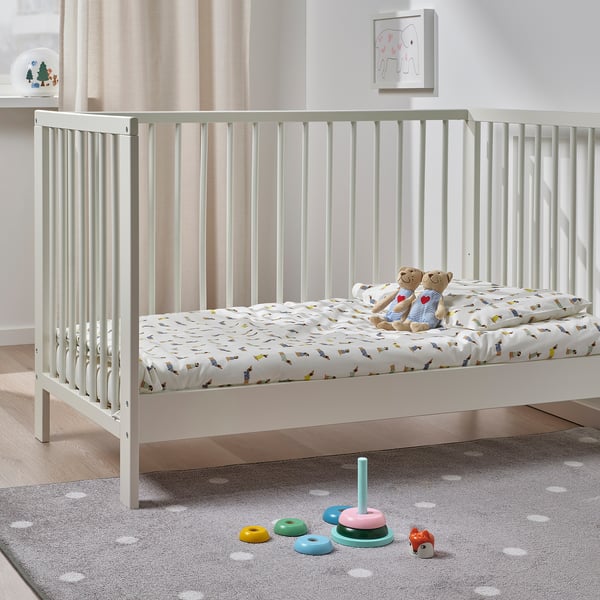 Babybett mit Teddybären, buntem Stapelspielzeug und gepunktetem Teppich. Kunstwerk an der Wand.