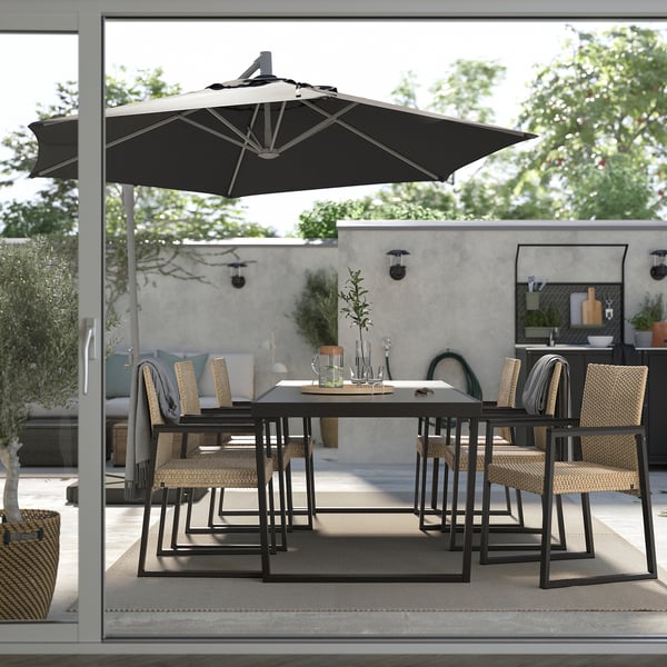 Modernes Esszimmer im Freien mit schwarzem Tisch und Stühlen unter einem großen Sonnenschirm. Perfekt für den Einsatz auf der Terrasse.
