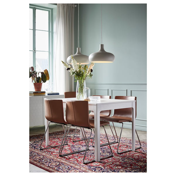 Modernes Esszimmer mit weißem Tisch, braunen Stühlen, Pendelleuchten, blauen Wänden, Fenster und Teppich.