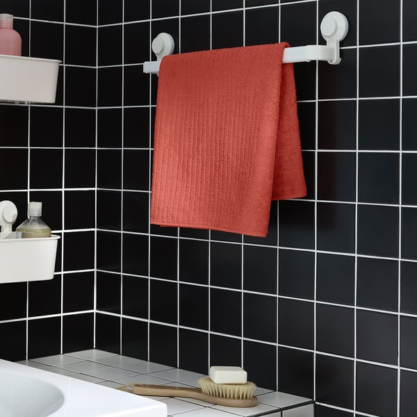 VÅGSJÖN rotes Handtuch hängt zwischen weißen Haken an einer dunkel gefliesten Wand. Klein, rechteckig, angrenzend an ein Waschbecken mit Pflegeprodukten.