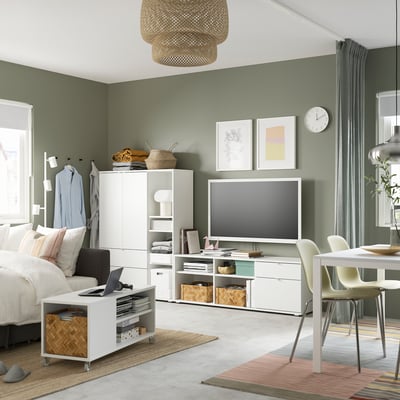 Modernes Wohnzimmer mit grünen Wänden, mit einem weißen VIHALS-TV-Ständer, einem gemütlichen Bett und einem runden Teppich.