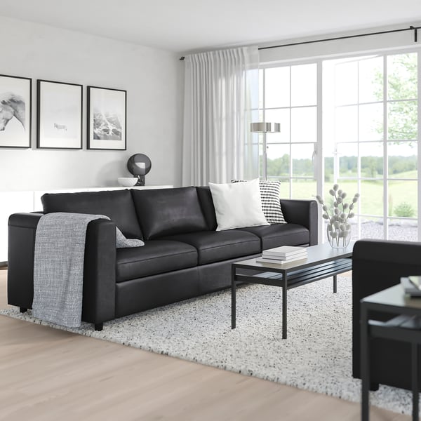 Modernes Wohnzimmer mit großem schwarzen VIMLE-Sofa, weißem Teppich, Couchtisch und großem Fenster.