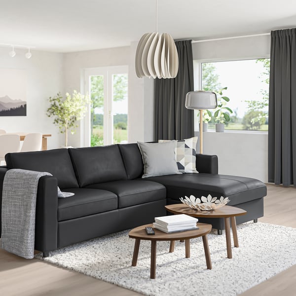 Modernes Wohnzimmer mit schwarzer VIMLE-Sektion, Holztischen, weißem Teppich und großem Fenster.