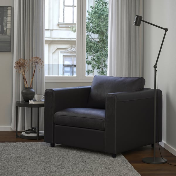 Schwarzer VIMLE Sessel im modernen Wohnzimmer mit Stehlampe und Tischdekoration.