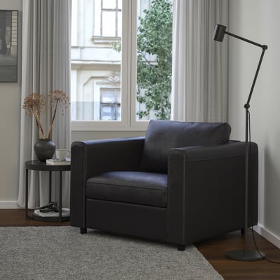 Schwarzer VIMLE Sessel im modernen Wohnzimmer mit Stehlampe und Tischdekoration.